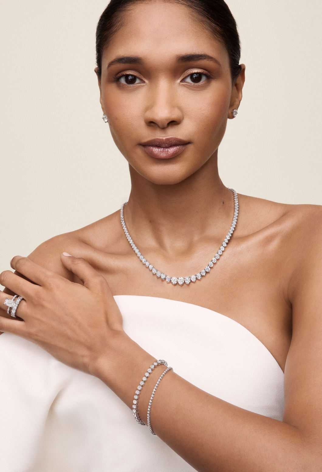 A closeup image of a female model looking at the camera showcasing diamond drop earrrings, necklace, tennis bracelet, enternity band and engagement ring A closeup image of a female model looking at the camera showcasing diamond drop earrrings, necklace, tennis bracelet, enternity band and engagement ring
